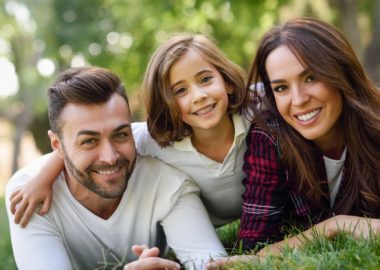 smiling-couple-lying-on-the-lawn-with-their-daughter_1139-618