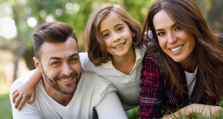 smiling-couple-lying-on-the-lawn-with-their-daughter_1139-618